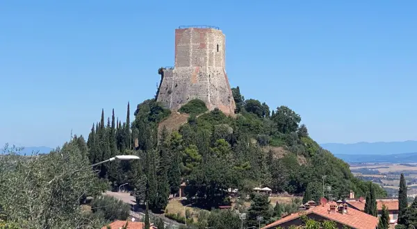 La rocca di Tentennano domina il paesaggio collinare toscano, circondata da cipressi e case con tetti rossi.