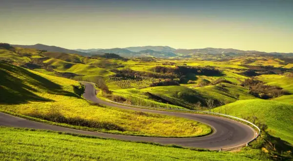 Strada volterrana serpeggia tra dolci colline verdi, un invito a esplorare paesaggi mozzafiato sotto un cielo limpido.