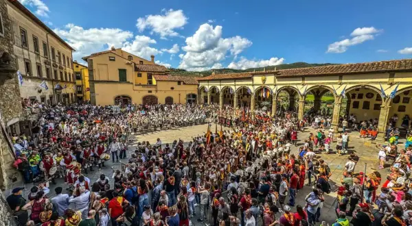 Folla in piazza per il palio dei rioni Castiglion Fiorentino, con figuranti in costume e bandiere.