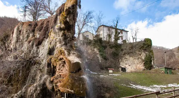Cascata calcarea presso le grotte di Labante, con case in collina e cielo azzurro.