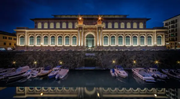Il mercato di Livorno illuminato di notte, con barche ormeggiate e il loro riflesso sull'acqua.