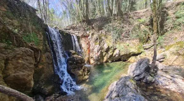 Cascata nel bosco, acque cristalline del fiume Merse che scendono tra rocce e vegetazione lussureggiante.