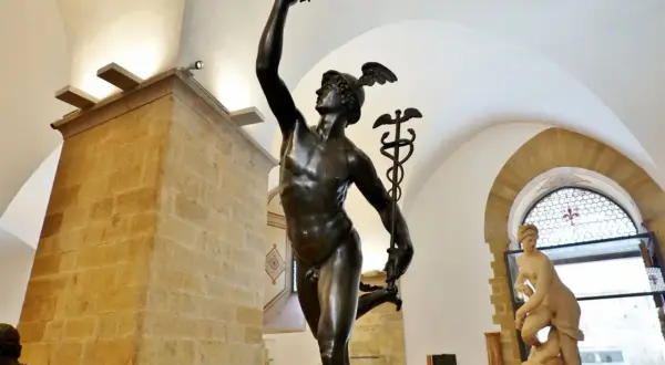 Mercurio in bronzo, un'opera che ricorda la grazia del David di Donatello. La statua, con il suo elmo alato, si staglia contro un soffitto ad arco.