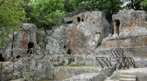 Antiche tombe scavate nella roccia, parte di siti etruschi, con sentieri e recinzioni in legno.