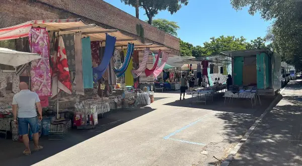 Mercato all'aperto a Grosseto, con bancarelle colorate di tessuti e abbigliamento sotto un cielo azzurro.