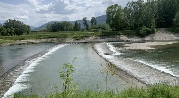 Il **parco fluviale del Serchio** offre uno spettacolo di acqua che scorre su dighe naturali, circondato da verdi colline e alberi rigogliosi sotto un cielo nuvoloso.