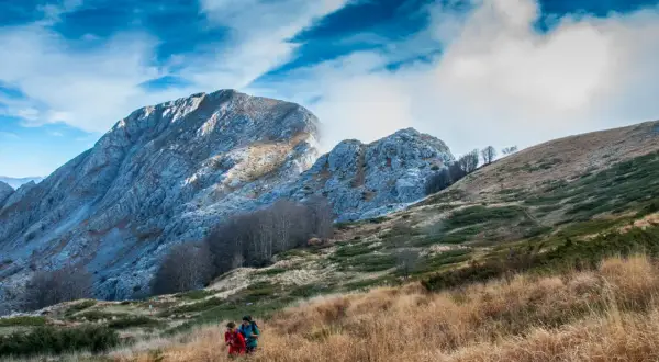 Due escursionisti attraversano un prato dorato, con le maestose Alpi Apuane sullo sfondo, un'esperienza di trekking tra i più belli.