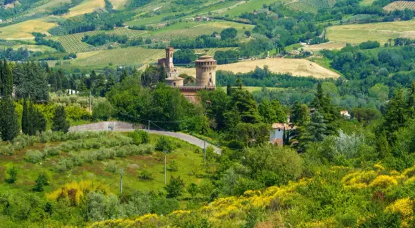 Colline verdi con un castello medievale e campi coltivati, tipiche delle strade panoramiche in Emilia Romagna.