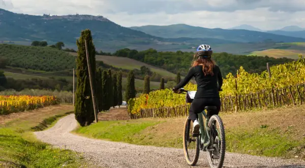 Donna in bici su strada sterrata tra vigneti e cipressi, con colline toscane sullo sfondo. Perfetti giri in bici toscana.
