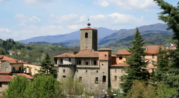 La Rocca Ariostesca domina il borgo con la sua torre imponente, circondata da case dai tetti rossi e verdi colline.