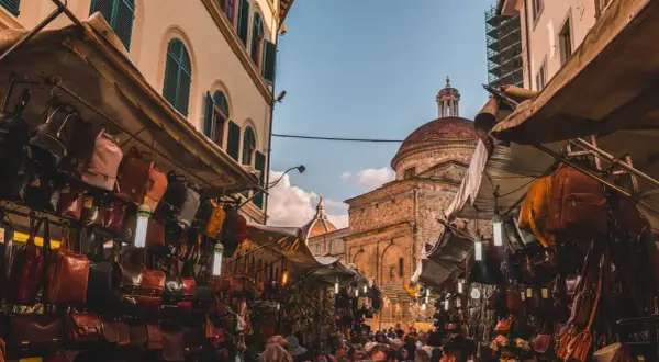 Mercato fiorentino con borse in pelle e cupole sullo sfondo, un assaggio della firenze non turistica.