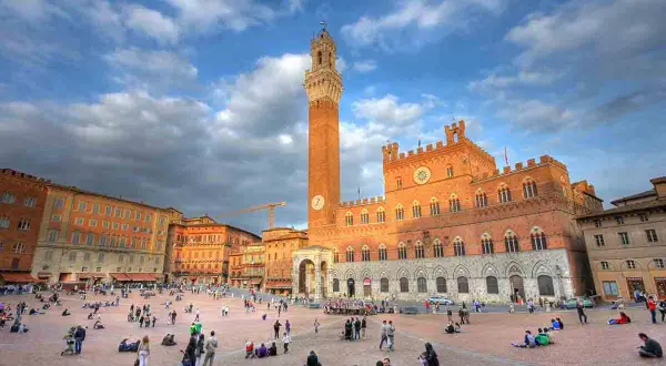 Piazza del Campo a Siena, un luogo iconico per il turismo, con il Palazzo Pubblico e la Torre del Mangia sotto un cielo nuvoloso.
