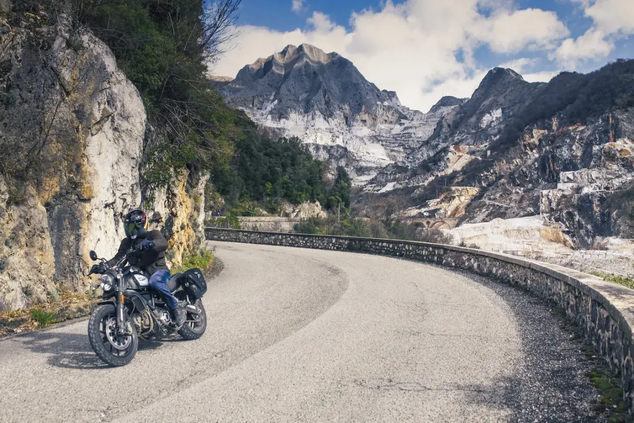 Motociclista su strada tortuosa con montagne di marmo sullo sfondo. Perfetto per itinerari moto Toscana 3 giorni.