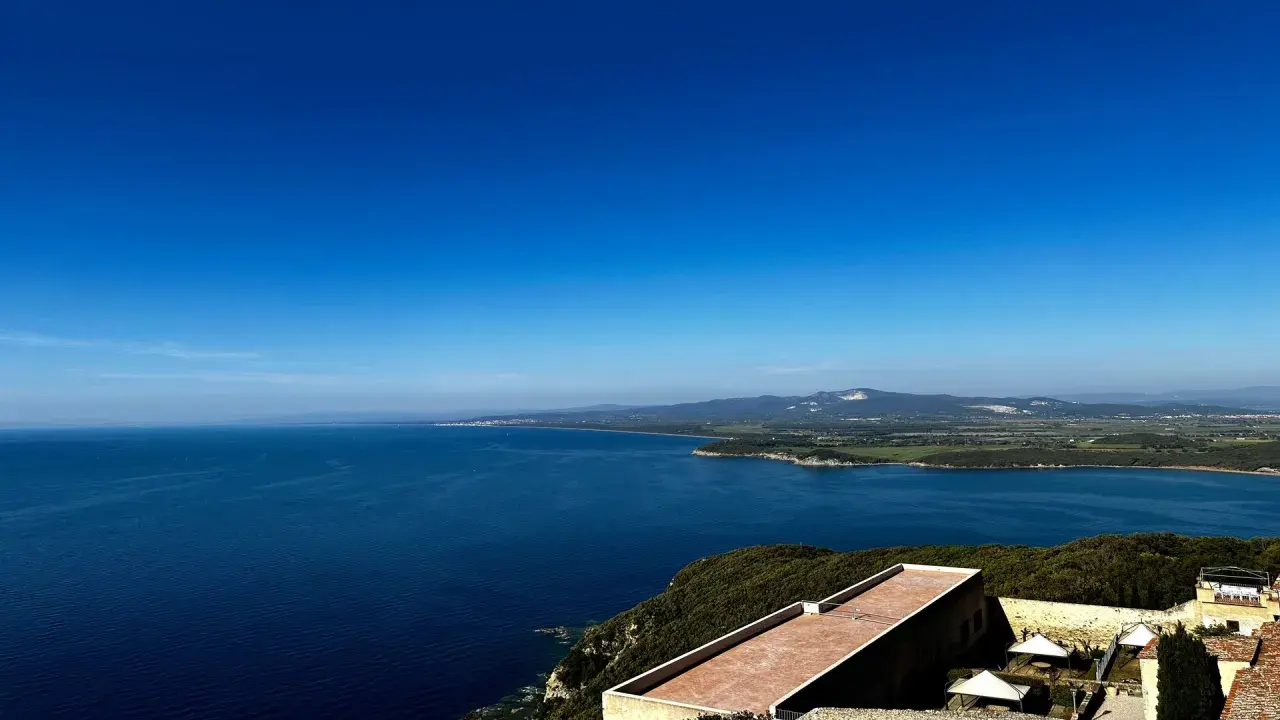 Vista panoramica sul mare blu intenso della Maremma, con colline verdi e un borgo antico. Perfetto per scoprire cosa vedere in Maremma.