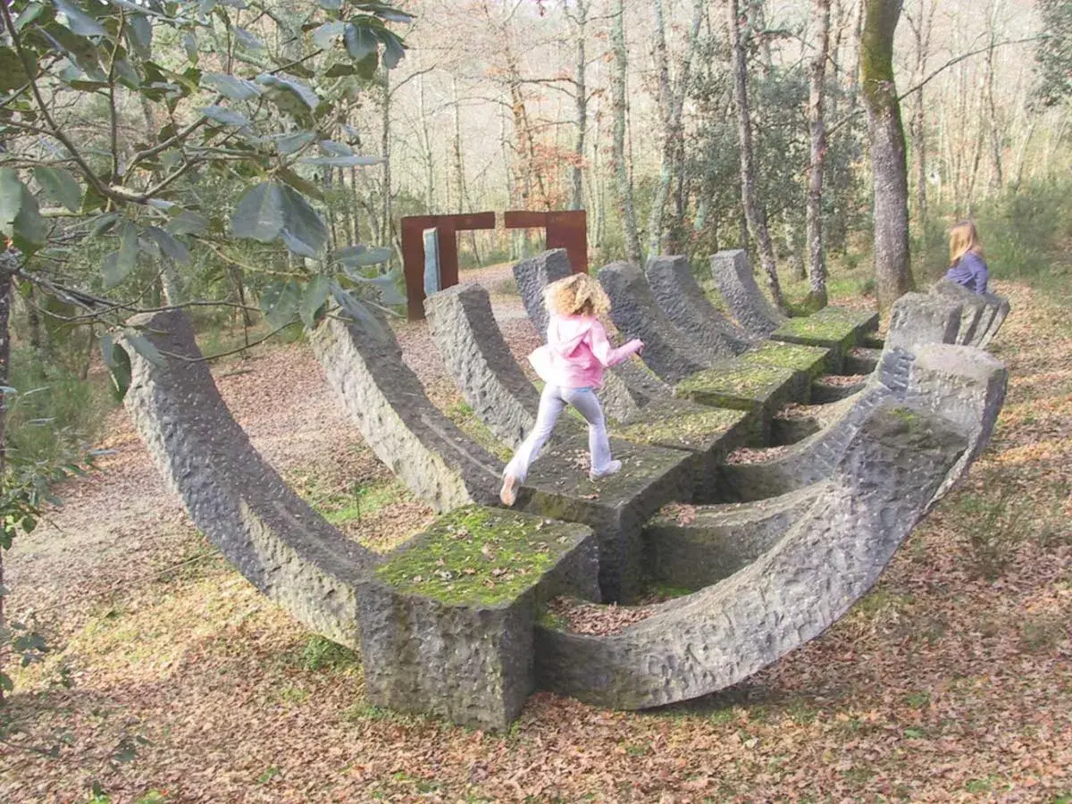 Bambini esplorano un **museo a cielo aperto in Toscana**, tra sculture in pietra e alberi secolari.