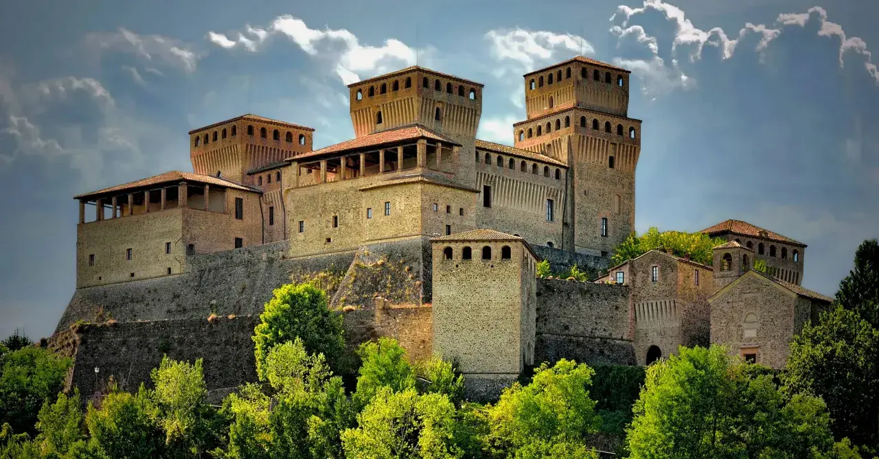 Rocche imponenti e torri medievali, tra i borghi vicino Parma, si stagliano contro un cielo nuvoloso, circondate da un verde lussureggiante.