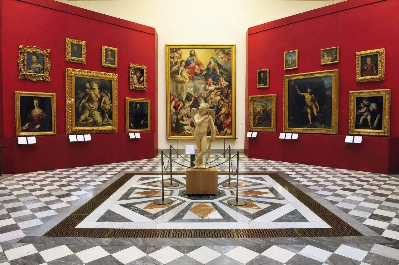 Sala con opere d'arte nei musei d'arte a Firenze. Statua di Cupido al centro, circondata da dipinti su pareti rosse.