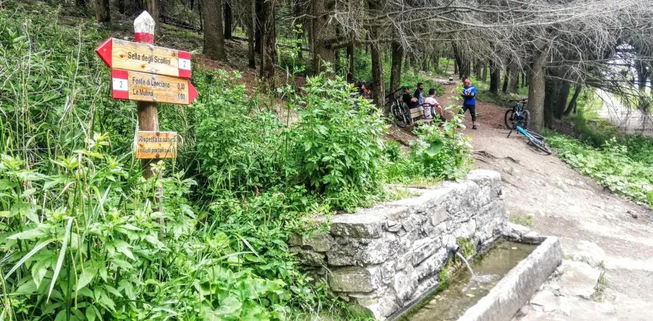 Segnavia per il trekking sul Monte Morello, con ciclisti che riposano vicino a una fontana.