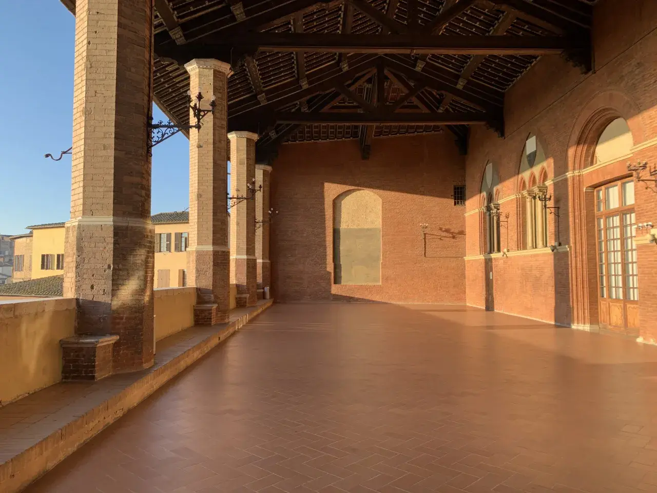 La loggia dei Nove a Siena, con le sue colonne in cotto e il tetto a capriate, baciata dalla luce dorata del tramonto.
