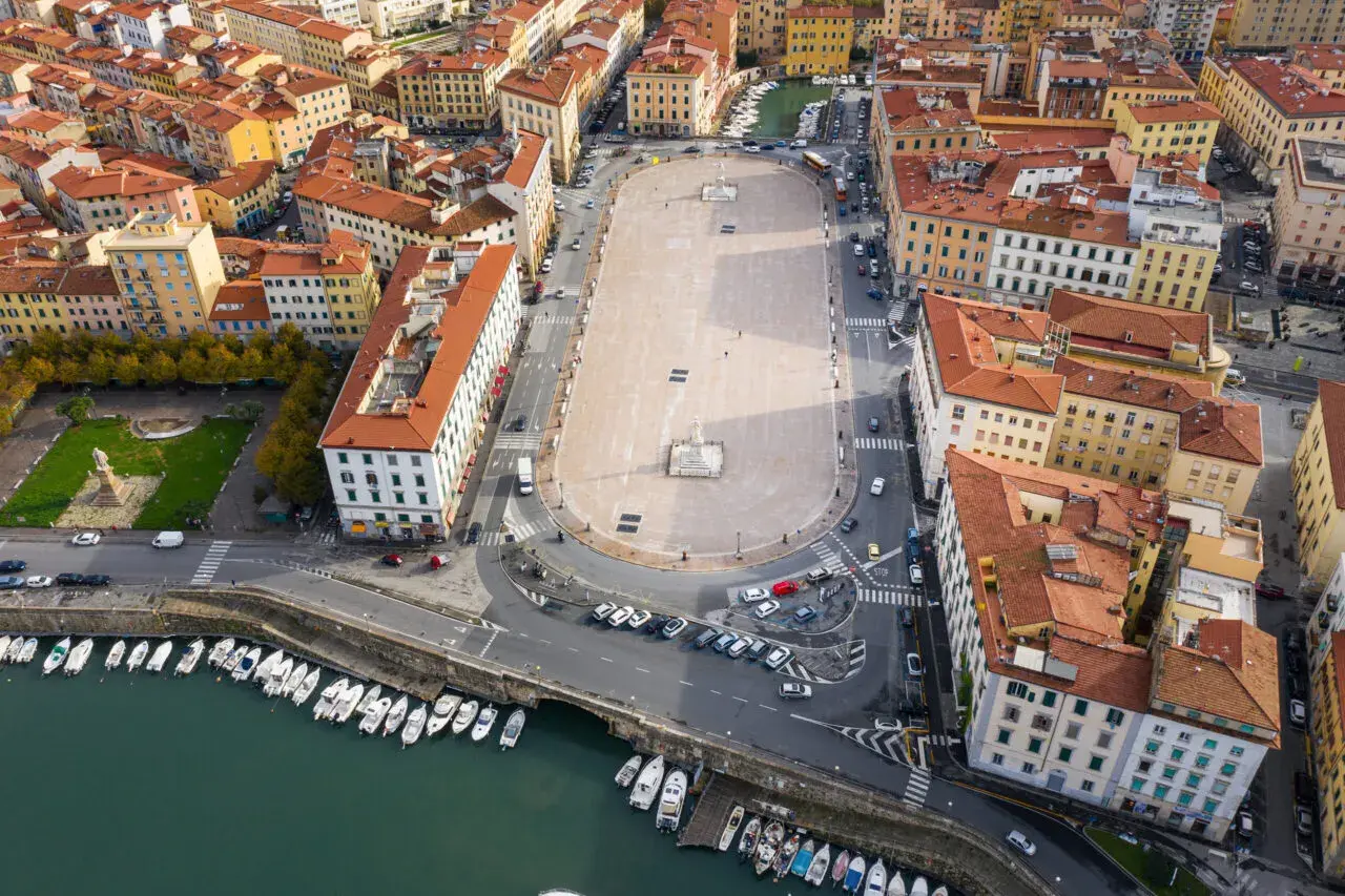 Vista aerea della piazza della Repubblica a Livorno, con edifici storici, un monumento centrale e barche ormeggiate nel canale.