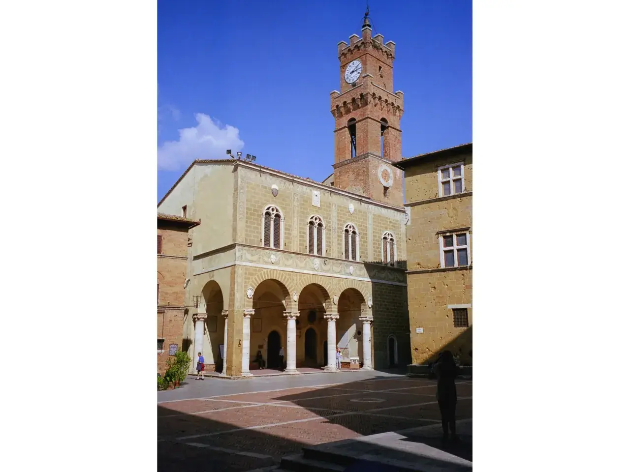 Il **Palazzo Comunale di Pienza** domina la piazza con la sua torre dell'orologio. Archi eleganti e finestre gotiche caratterizzano l'edificio.