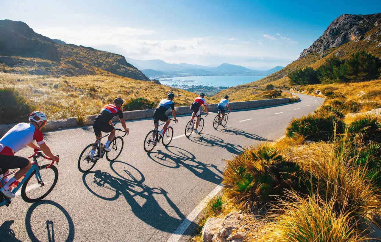 Ciclisti su strada panoramica, ideali per itinerari bici 3 giorni. Paesaggio montuoso e mare sullo sfondo.