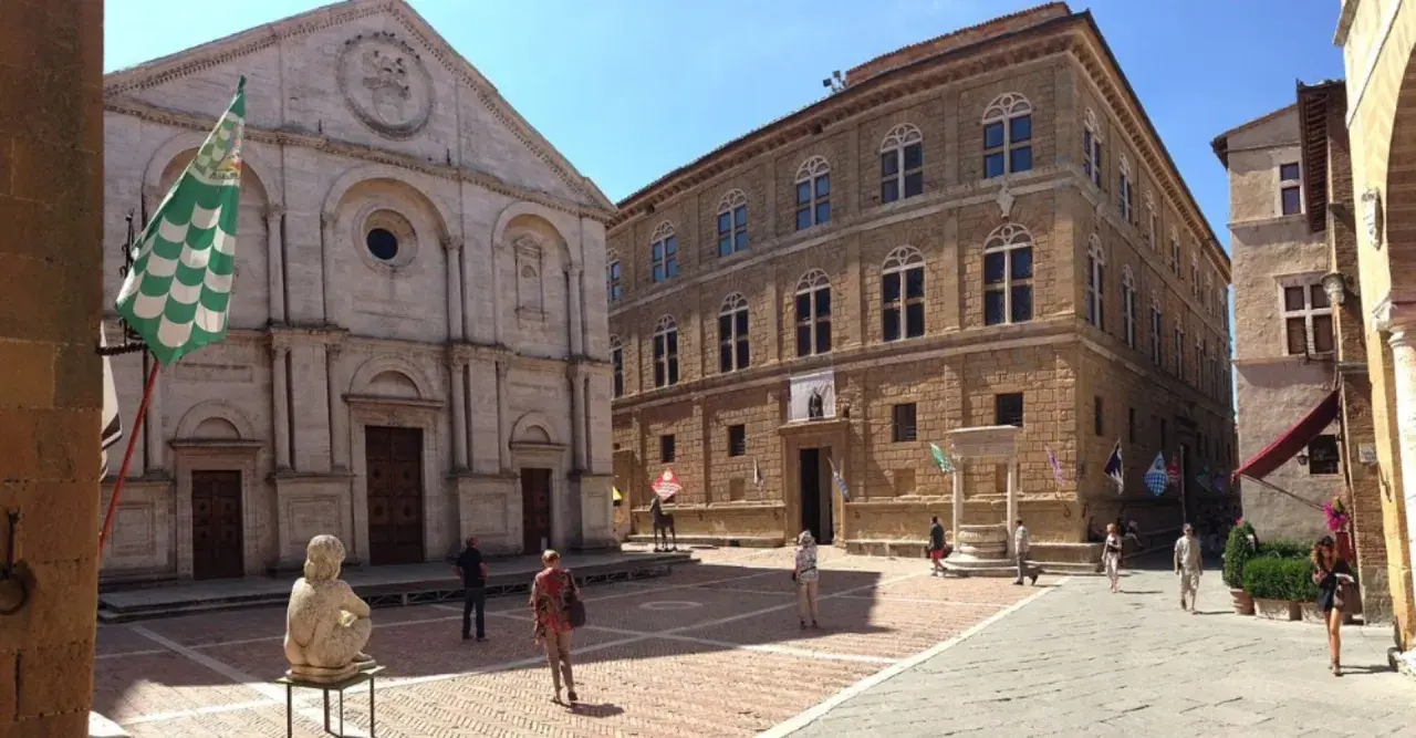 La **Pienza piazza** è un luogo incantevole con un duomo imponente e palazzi rinascimentali. Una scultura e bandiere colorate aggiungono vivacità.