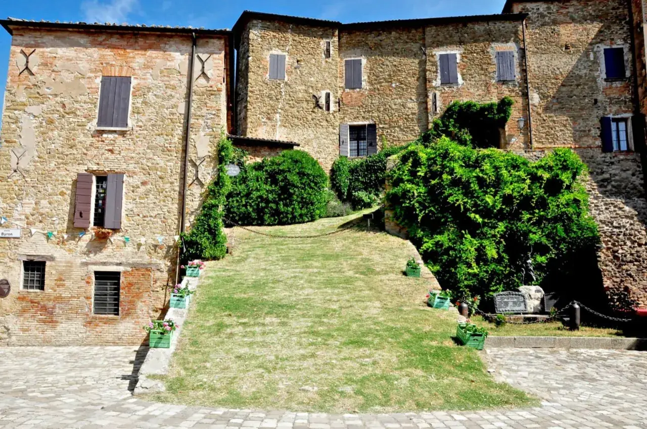 Antico borgo di Monteleone di Roncofreddo, con case in pietra e mattoni, finestre con persiane e un prato verde.