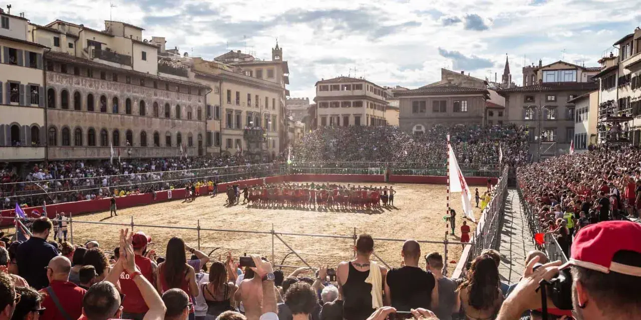 Un campo di sabbia a Firenze, gremito di spettatori, ospita un'intensa partita di calcio storico.