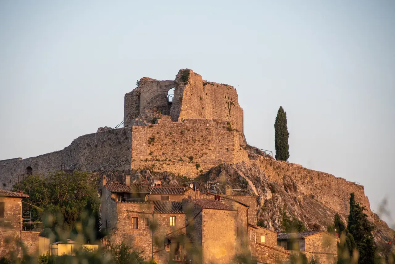 Rocca Aldobrandesca a Castiglione d'Orcia, un antico maniero in pietra che domina il borgo, con un cipresso solitario a vegliare.