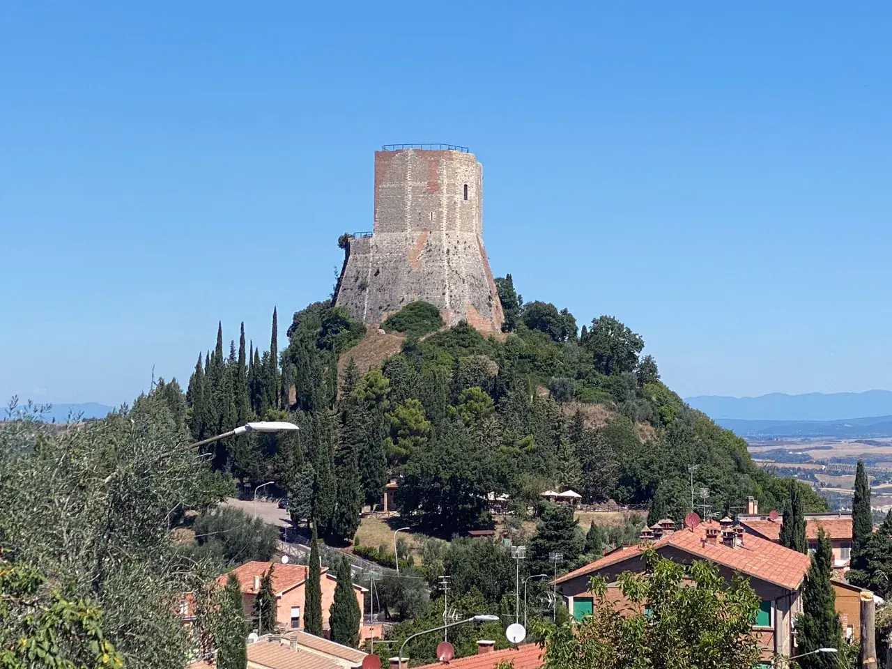 La rocca di Tentennano domina il paesaggio collinare toscano, circondata da cipressi e case con tetti rossi.