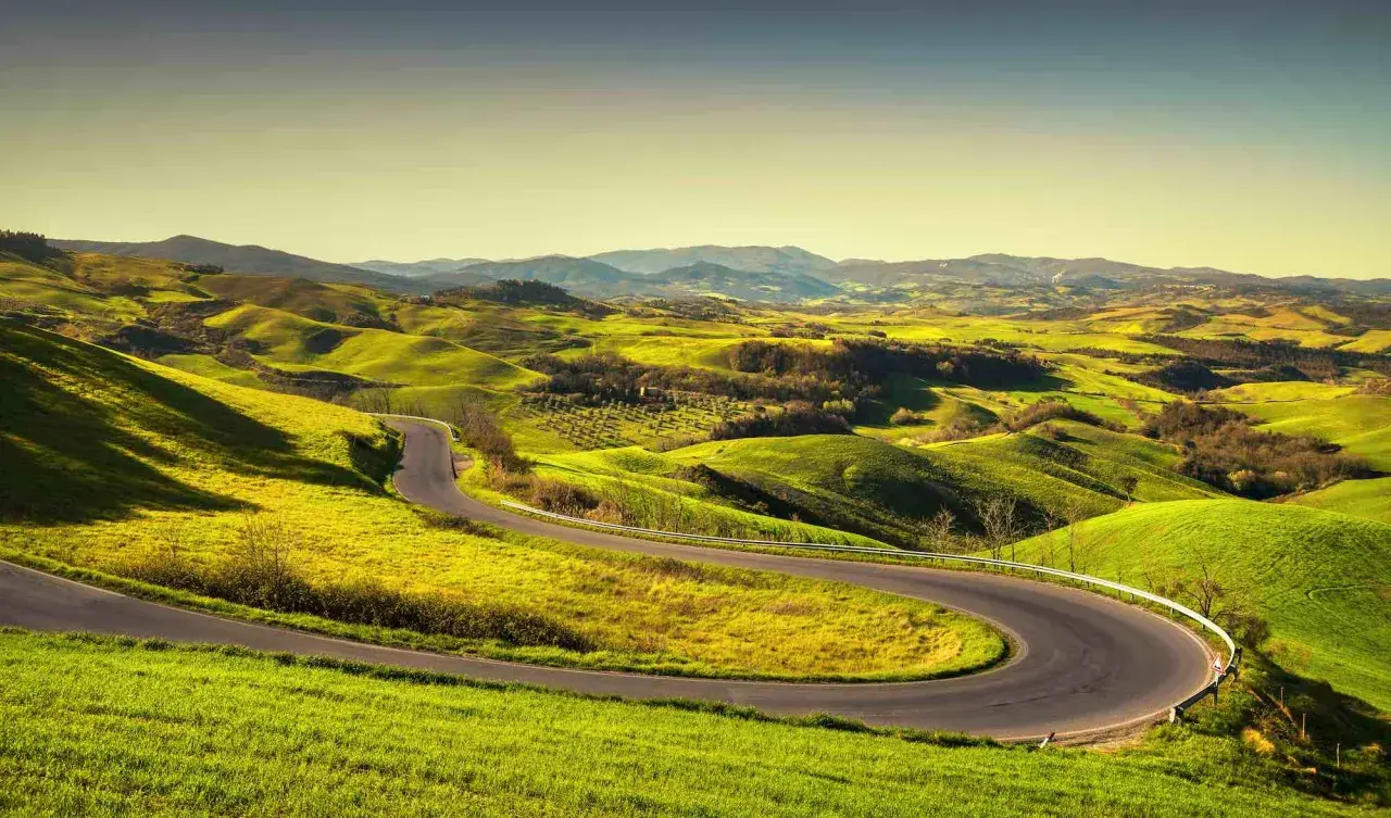 Strada volterrana serpeggia tra dolci colline verdi, un invito a esplorare paesaggi mozzafiato sotto un cielo limpido.