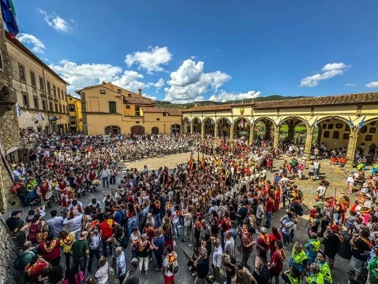 Folla in piazza per il palio dei rioni Castiglion Fiorentino, con figuranti in costume e bandiere.