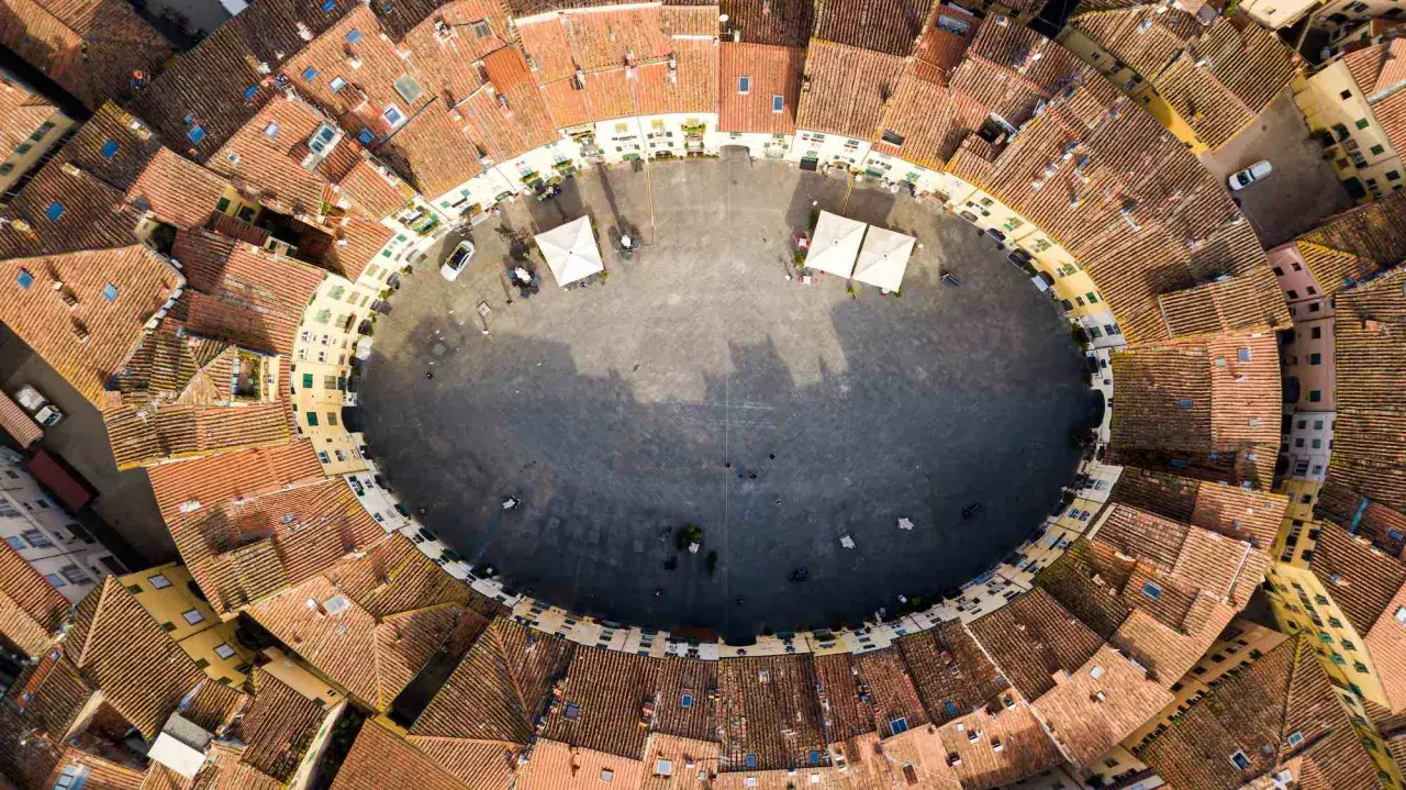 Vista aerea della **Piazza Anfiteatro** di Lucca, con i suoi caratteristici edifici ovali e i tetti rossi che la circondano.
