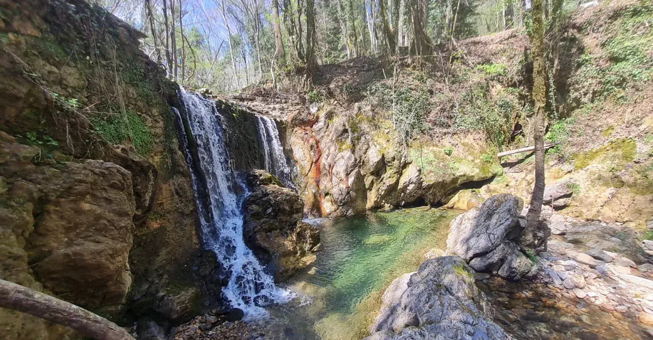 Cascata nel bosco, acque cristalline del fiume Merse che scendono tra rocce e vegetazione lussureggiante.