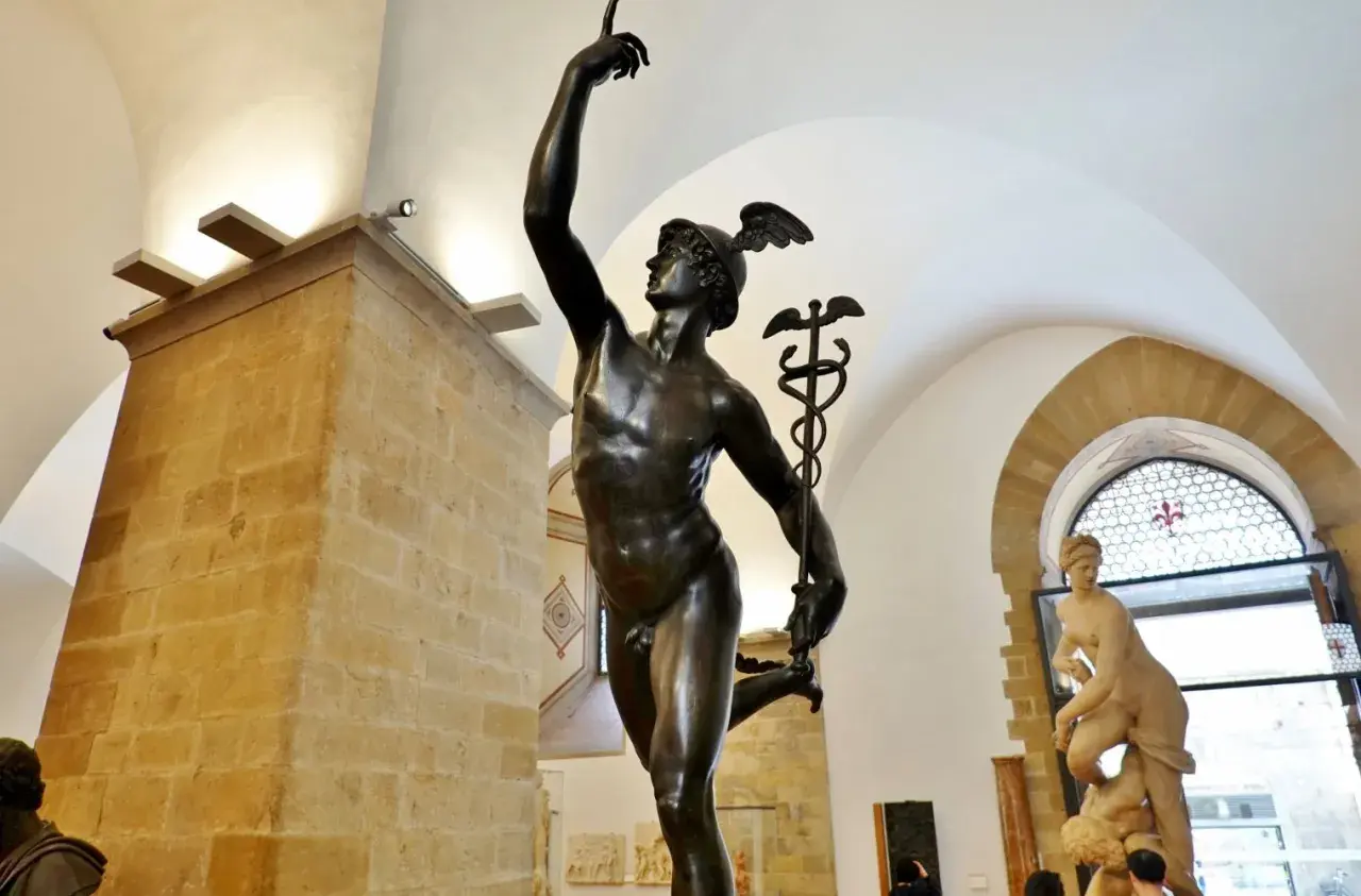 Mercurio in bronzo, un'opera che ricorda la grazia del David di Donatello. La statua, con il suo elmo alato, si staglia contro un soffitto ad arco.
