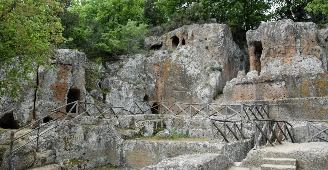 Antiche tombe scavate nella roccia, parte di siti etruschi, con sentieri e recinzioni in legno.