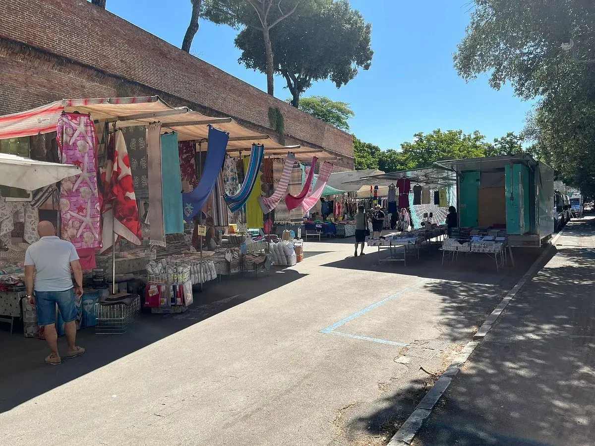 Mercato all'aperto a Grosseto, con bancarelle colorate di tessuti e abbigliamento sotto un cielo azzurro.