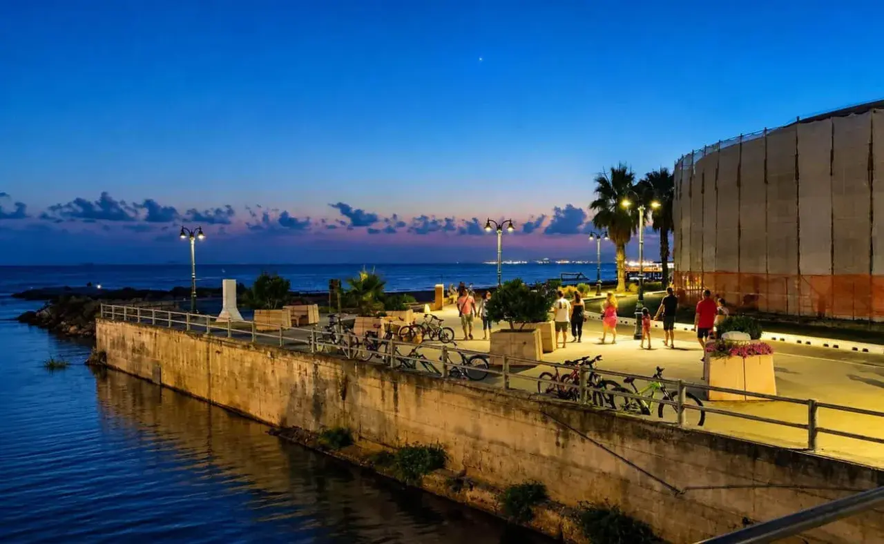Passeggiata serale lungo il mare a Follonica, con persone che camminano e biciclette parcheggiate.