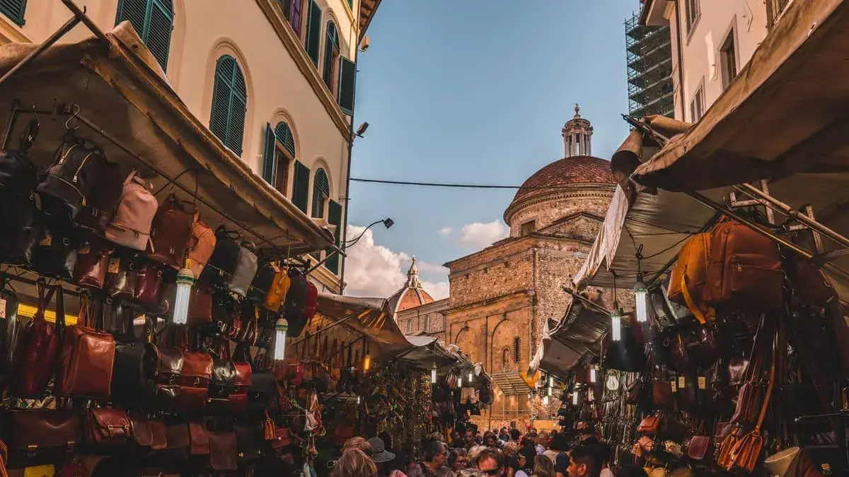 Mercato fiorentino con borse in pelle e cupole sullo sfondo, un assaggio della firenze non turistica.