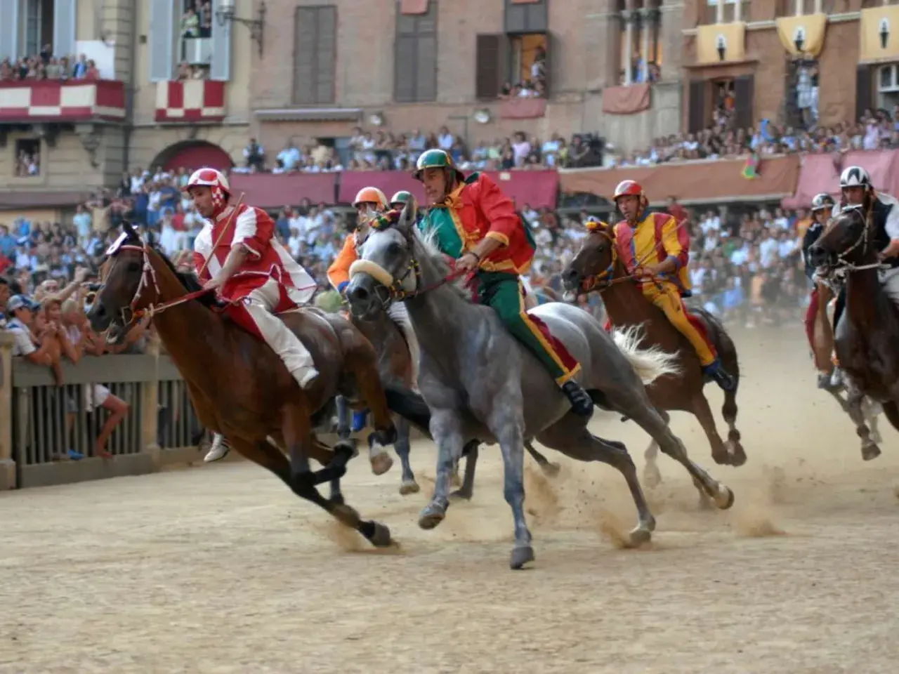 Cavalli e fantini in gara durante il Palio di Siena. La polvere si solleva mentre i cavalli corrono verso la vittoria.