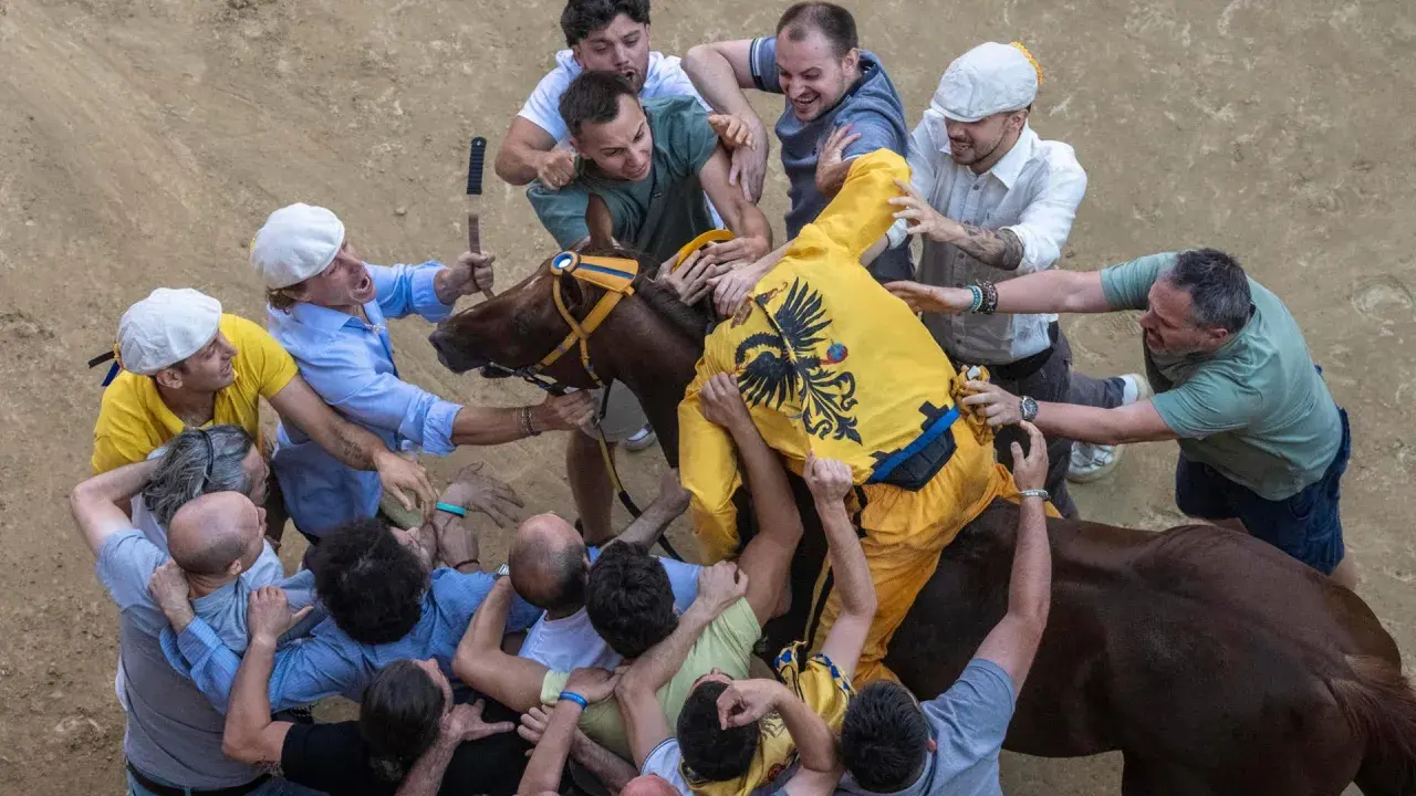 Caos e passione al Palio di Siena: uomini lottano per il cavallo, mostrando l'intensità delle regole non scritte di questa storica corsa.