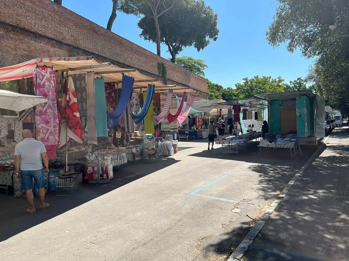 Mercato all'aperto a Grosseto, con bancarelle colorate di tessuti e abbigliamento sotto un cielo azzurro.