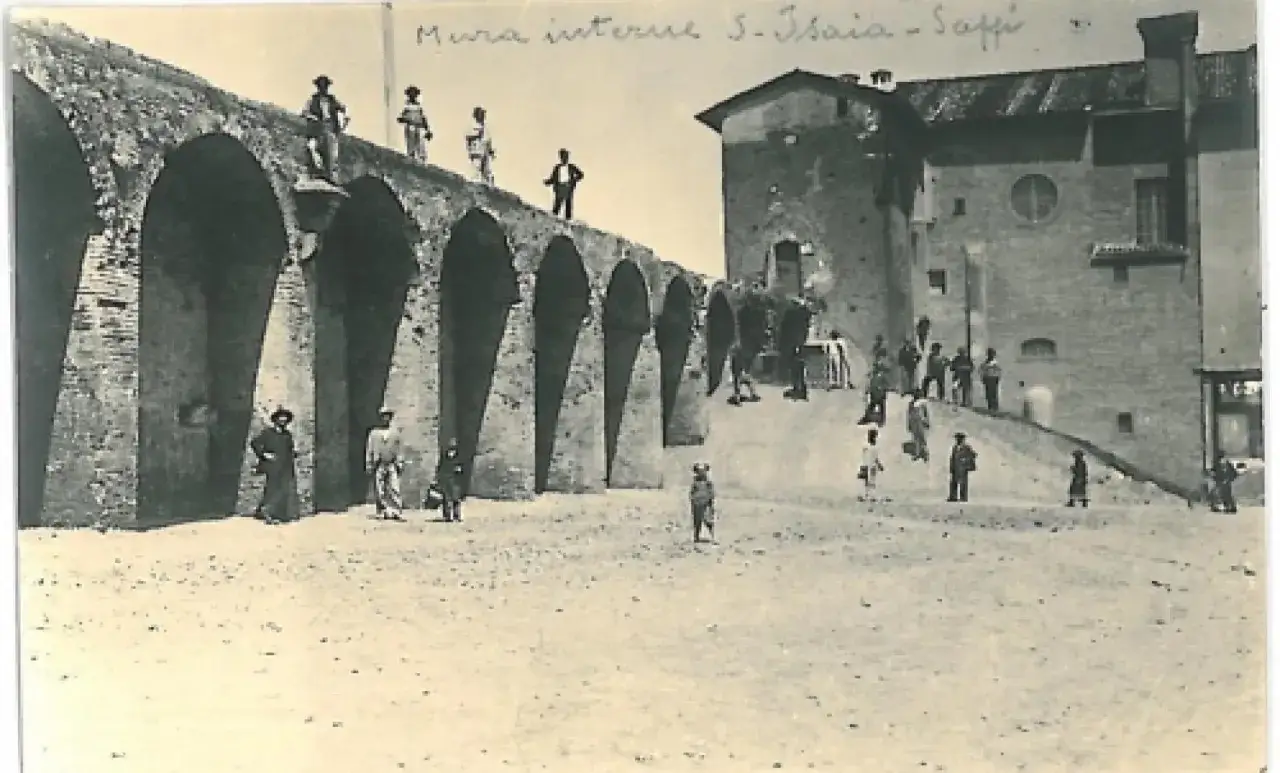Antiche porte di Bologna, con persone che passeggiano lungo le mura e un edificio storico sullo sfondo.