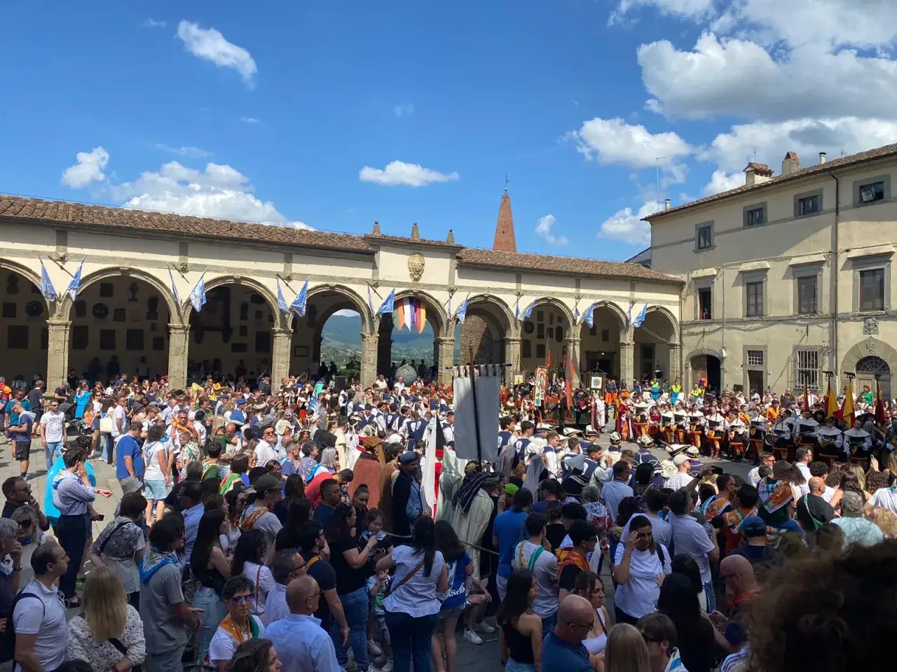 Folla in piazza per il palio dei rioni Castiglion Fiorentino, con figuranti in costume storico e bandiere.
