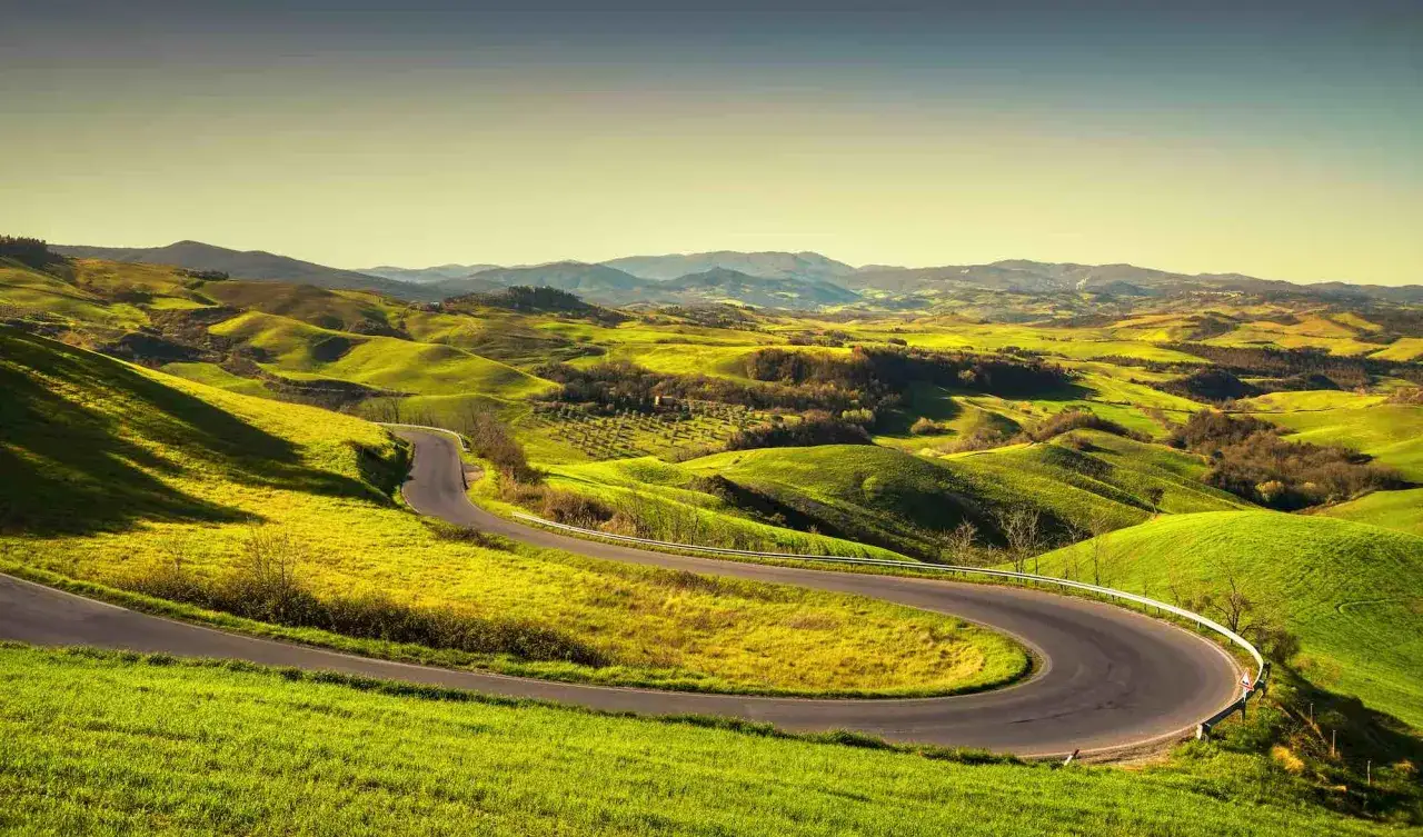Strada volterrana serpeggia tra dolci colline verdi, un invito a esplorare paesaggi mozzafiato sotto un cielo limpido.