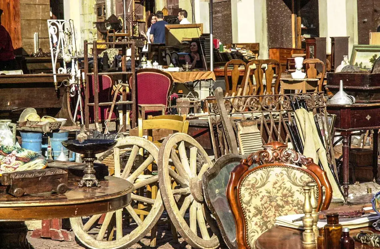 Un vivace mercatino antiquariato pieno di mobili antichi, ruote di carro, sedie decorate e oggetti d'epoca.