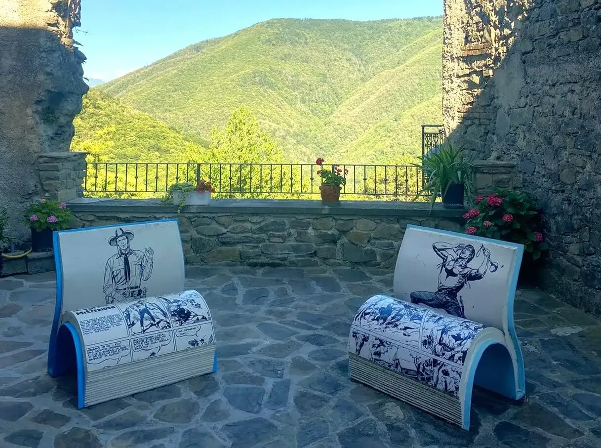 Montereggio, paese dei librai, accoglie con sedie a forma di libro e fumetti, con vista su colline verdi.