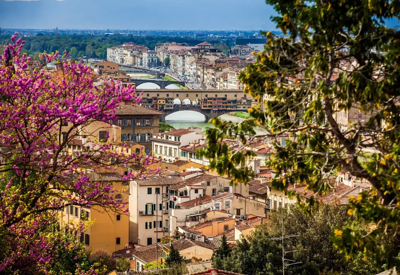 Vista panoramica di Firenze con Ponte Vecchio e alberi in fiore, uno dei tanti posti da visitare a Firenze.