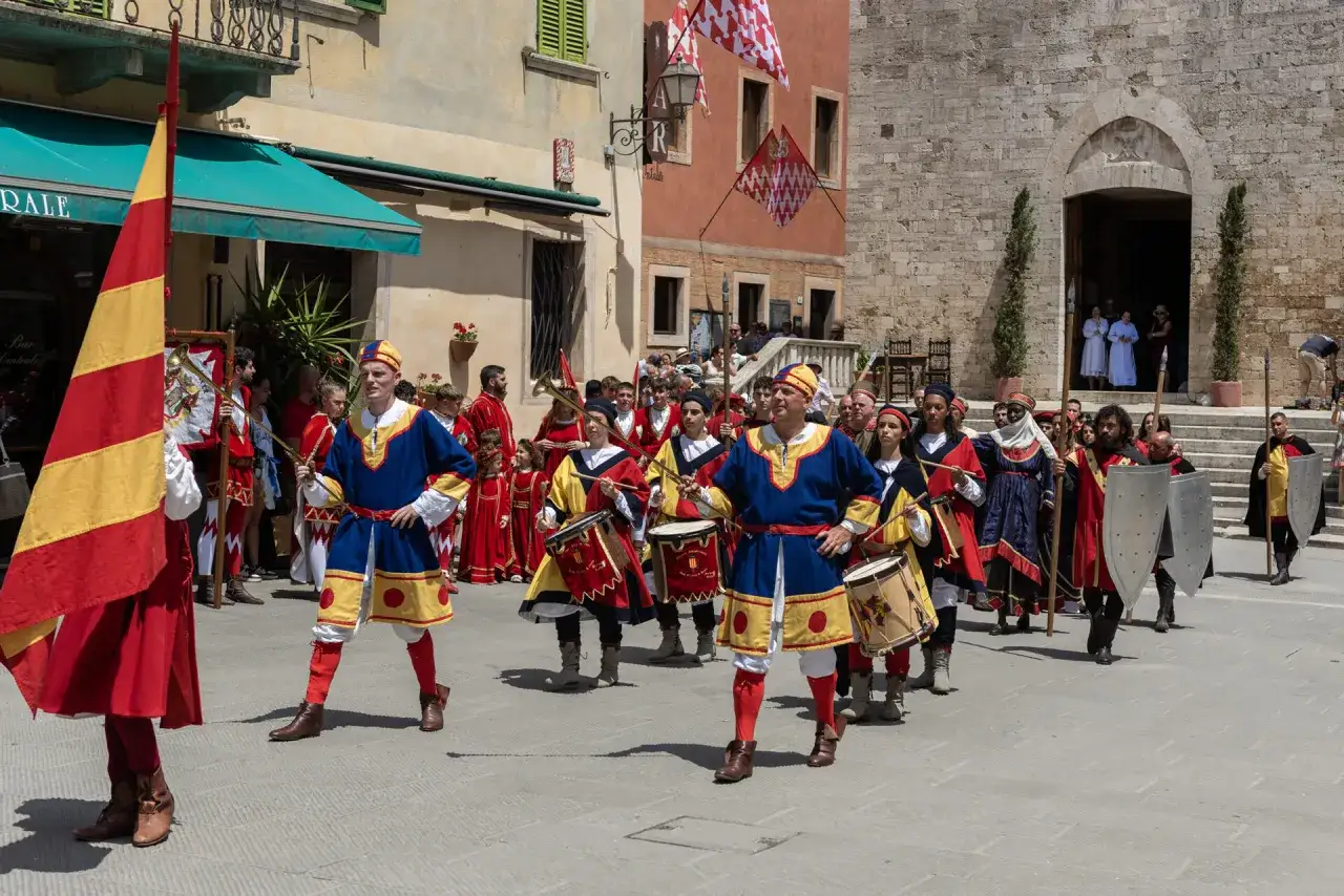 Sfilata in costume a San Quirico d'Orcia per il Barbarossa. Uomini in abiti storici sfilano con tamburi e bandiere.